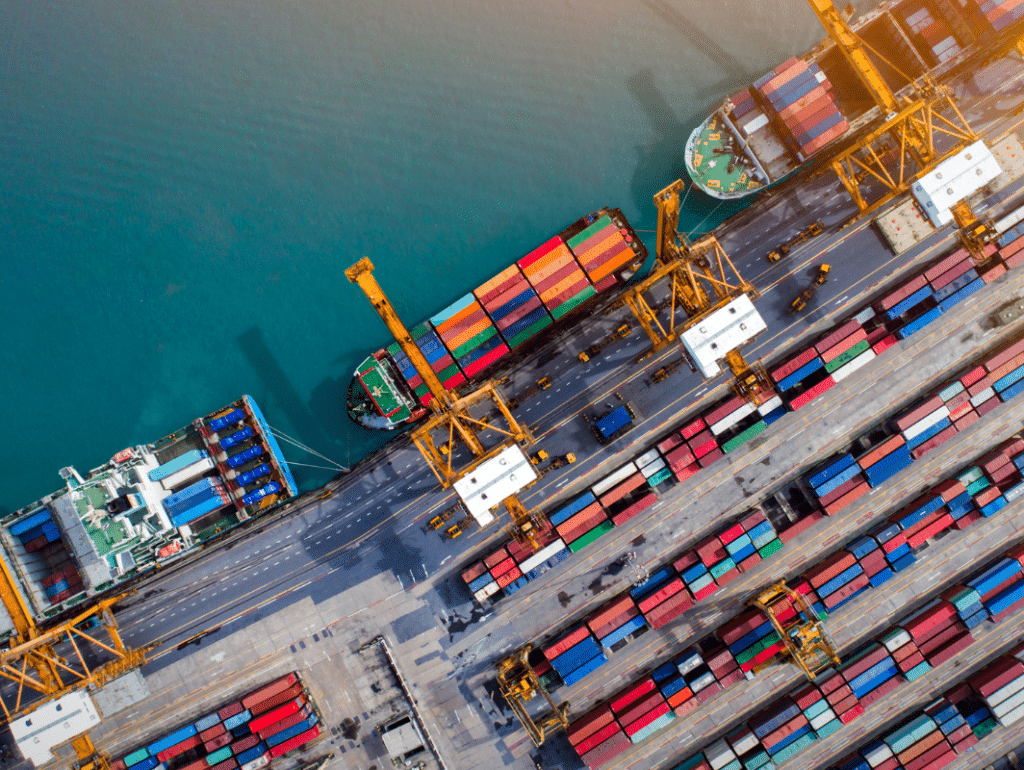 Aerial view of a busy port with colorful shipping containers and large cargo ships being loaded by yellow cranes—showcasing the dynamism central to E2E Supply Chain Ecosystem Transformation along the waterfront. EFESO Management Consultants