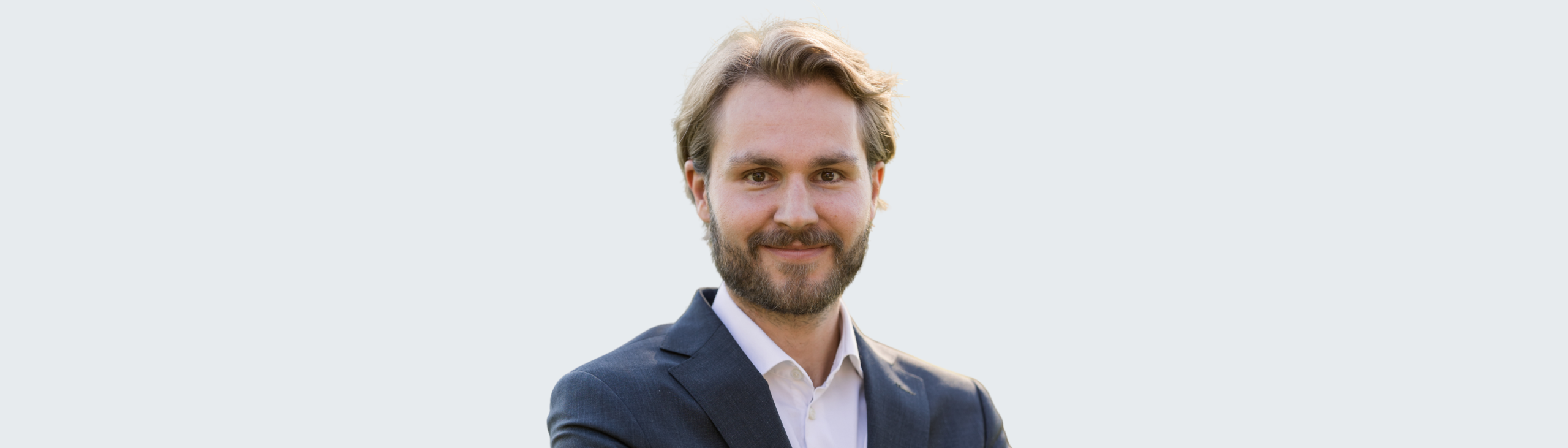 A man with light brown hair and a beard, wearing a dark suit jacket and white shirt, stands smiling with arms crossed against a plain light background, reflecting the confidence of the Leadership Team. EFESO Management Consultants