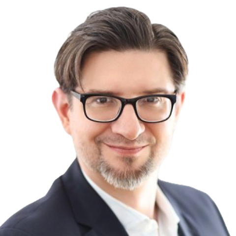 A man with short brown hair, glasses, and a goatee, wearing a dark suit jacket and white shirt, smiles at the camera against a plain light background reminiscent of forest hues. EFESO Management Consultants