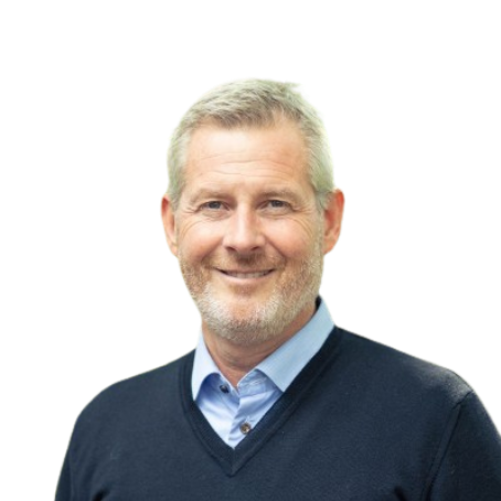 A middle-aged man with short gray hair and a beard is smiling. He is wearing a light blue collared shirt under a dark sweater, posed against a plain white background, as fresh as the air in a forest. EFESO Management Consultants